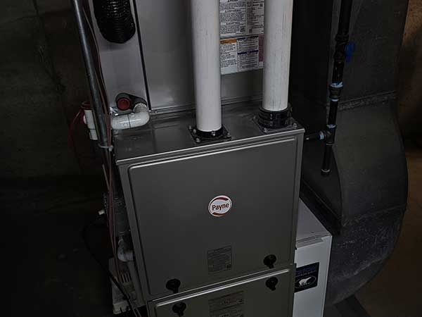 Gray furnace with white vent pipes in a utility closet, next to a black air duct.