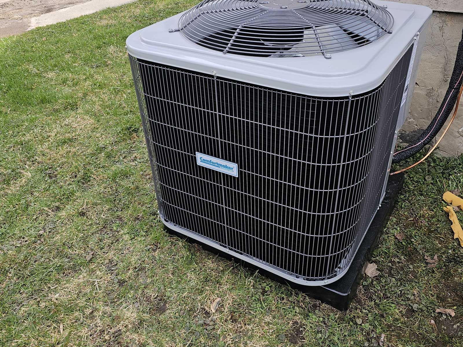 Outdoor air conditioner unit on grass, black and gray with a top fan grill