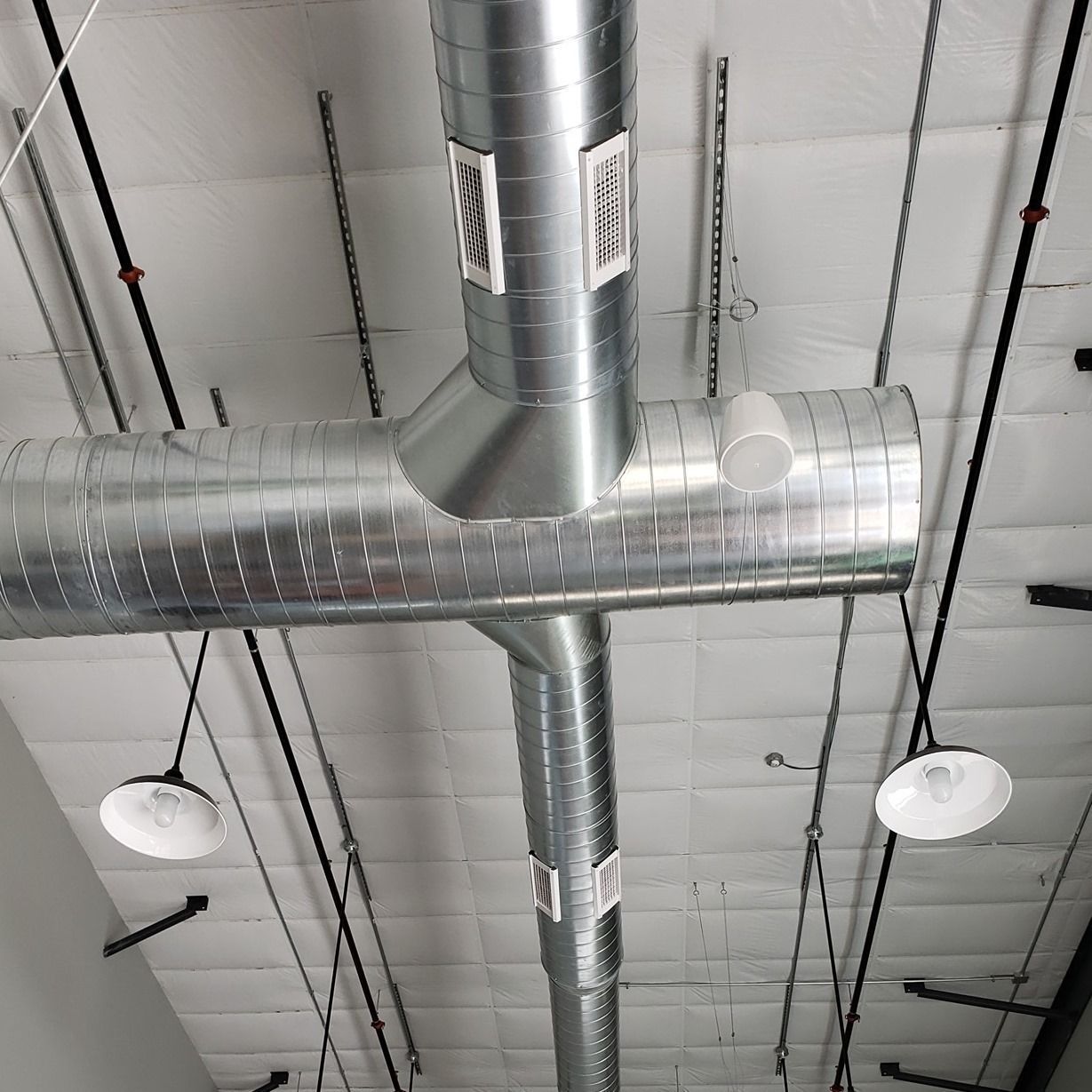 Industrial ceiling with silver HVAC ducts, white hanging lights, and black support cables