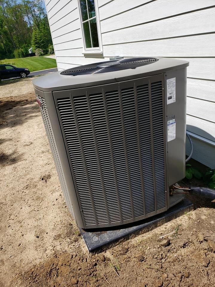 Outdoor air conditioner condenser unit beside a white house on a dirt foundation
