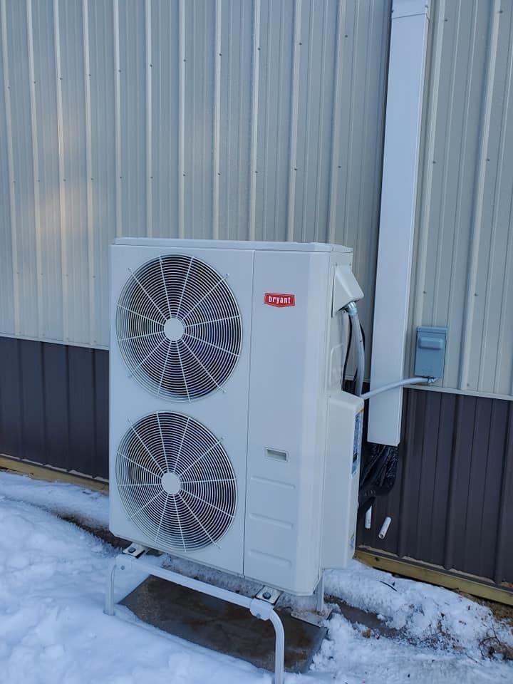 Outdoor heat pump unit with two fans mounted beside a corrugated metal wall in snow.