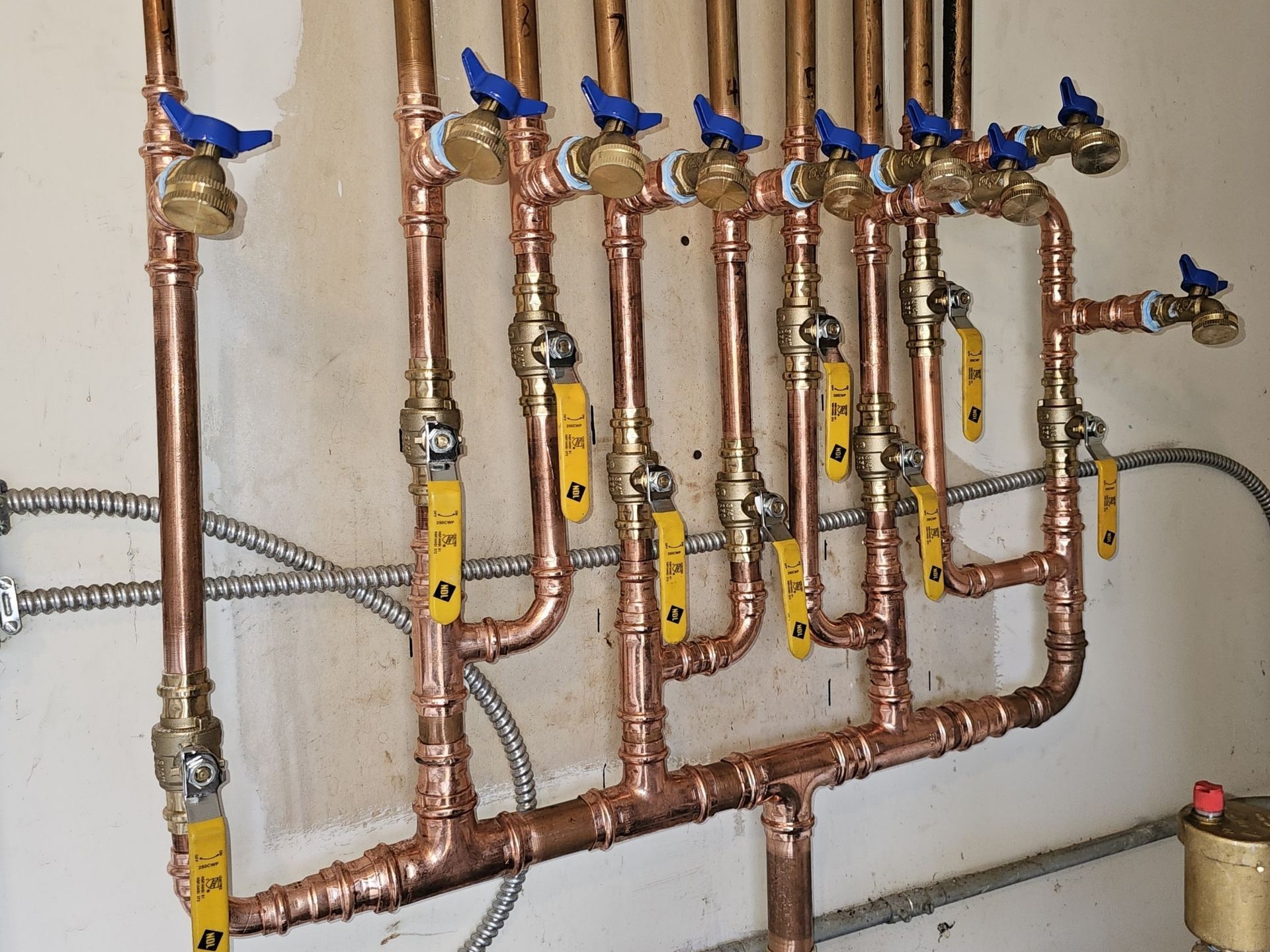 Copper pipes and yellow valves mounted on a wall in a plumbing manifold setup