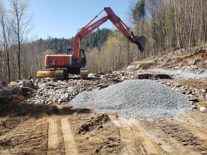 Excavator working on a gravel road at a wooded construction site