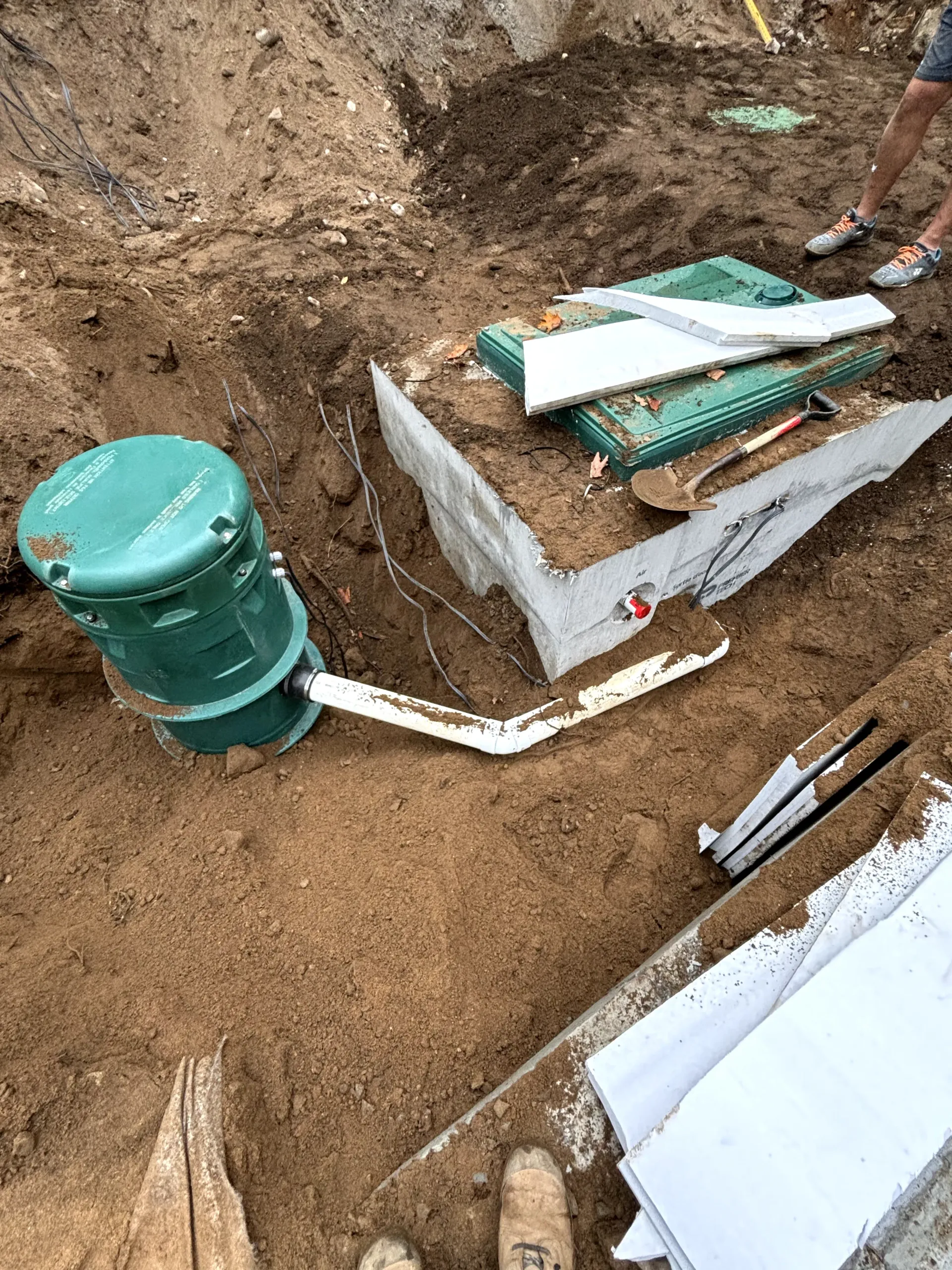 Underground utility box and green pipe connected by conduit in a dirt excavation area