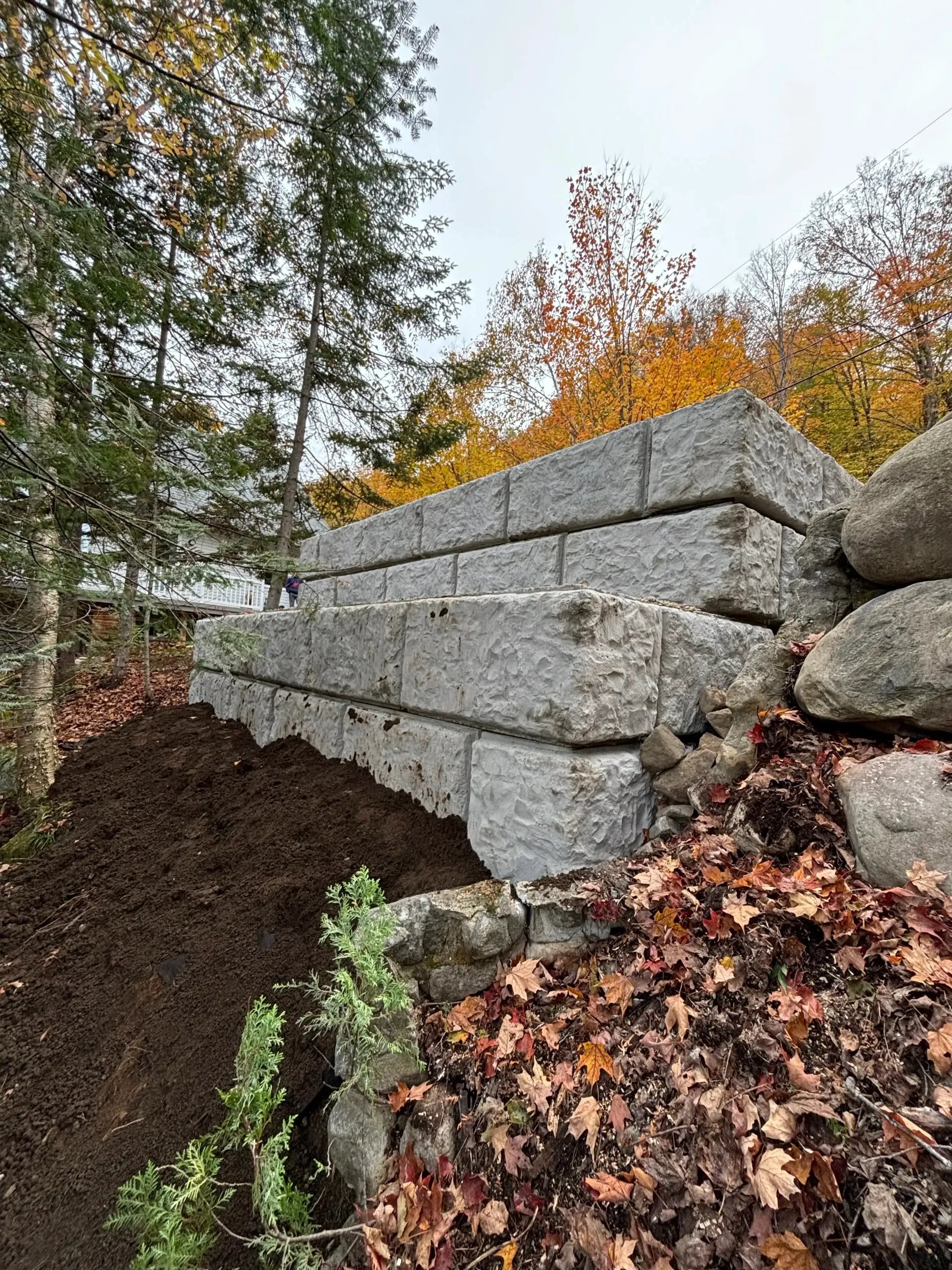 Stacked gray concrete blocks beside a muddy slope with autumn leaves and trees