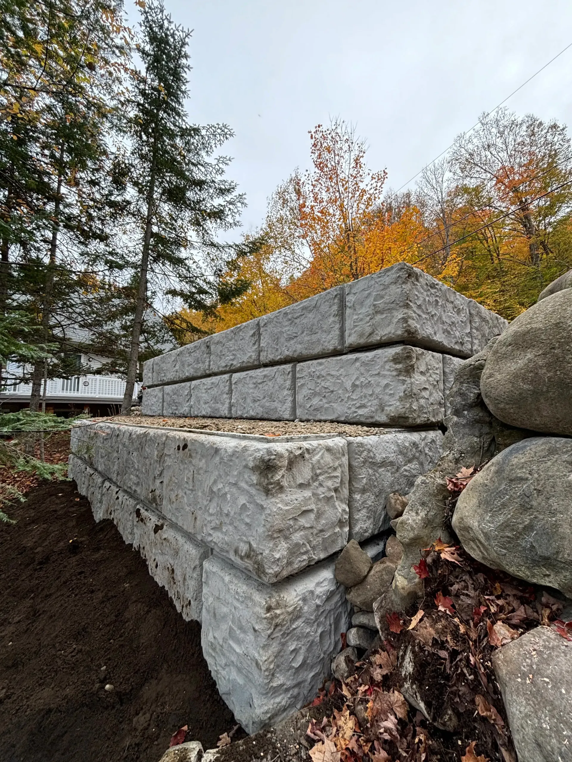 Concrete retaining wall blocks on a sloped landscape with autumn trees in the background