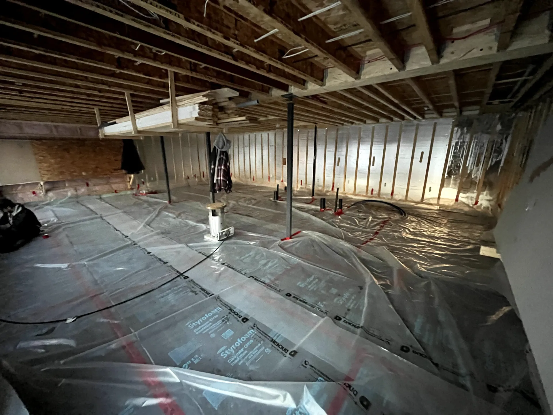 Unfinished basement with exposed joists, insulation, and plastic sheeting over the concrete floor.