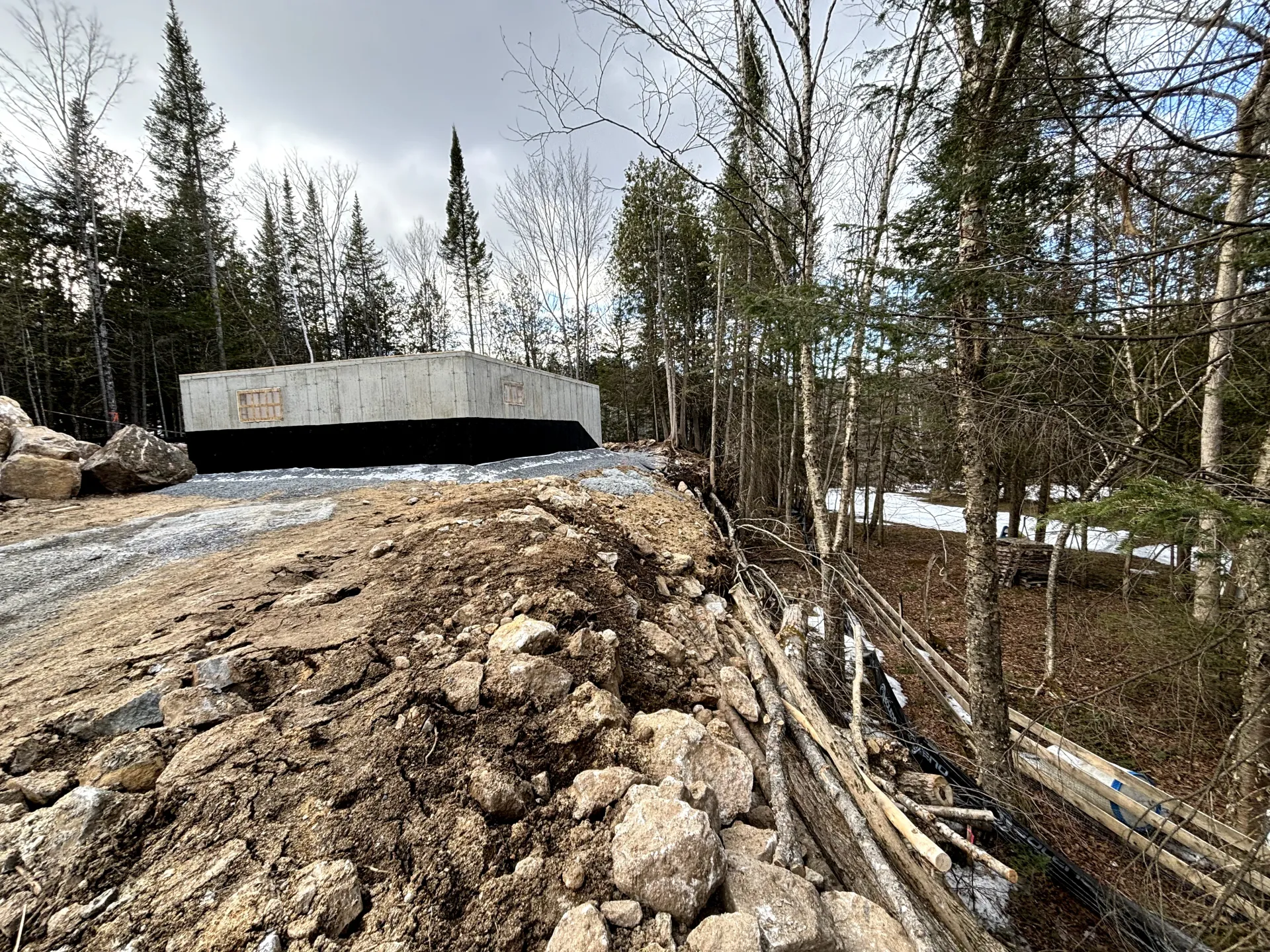 Dirt road leading to a concrete bridge in a wooded, snowy landscape