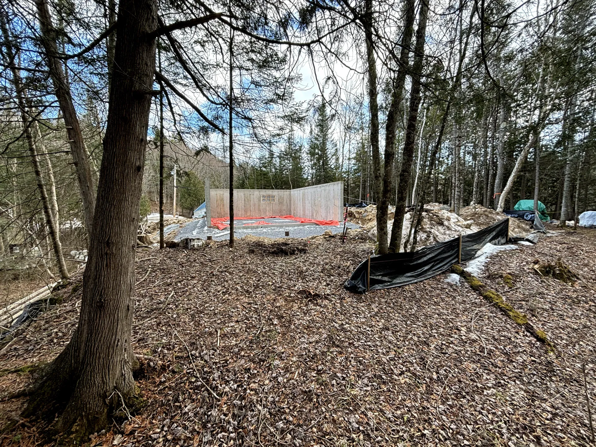 Excavator working on a rocky dirt road beside a pile of gravel in a wooded area