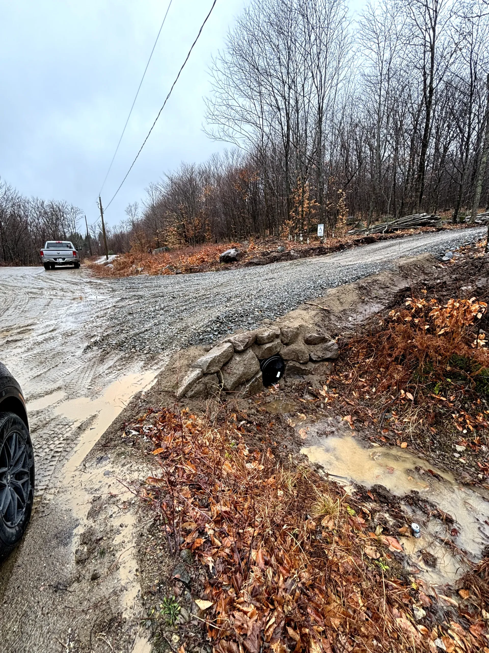 Mudslides cover a snowy rural road beside bare trees, with a truck approaching from the left.