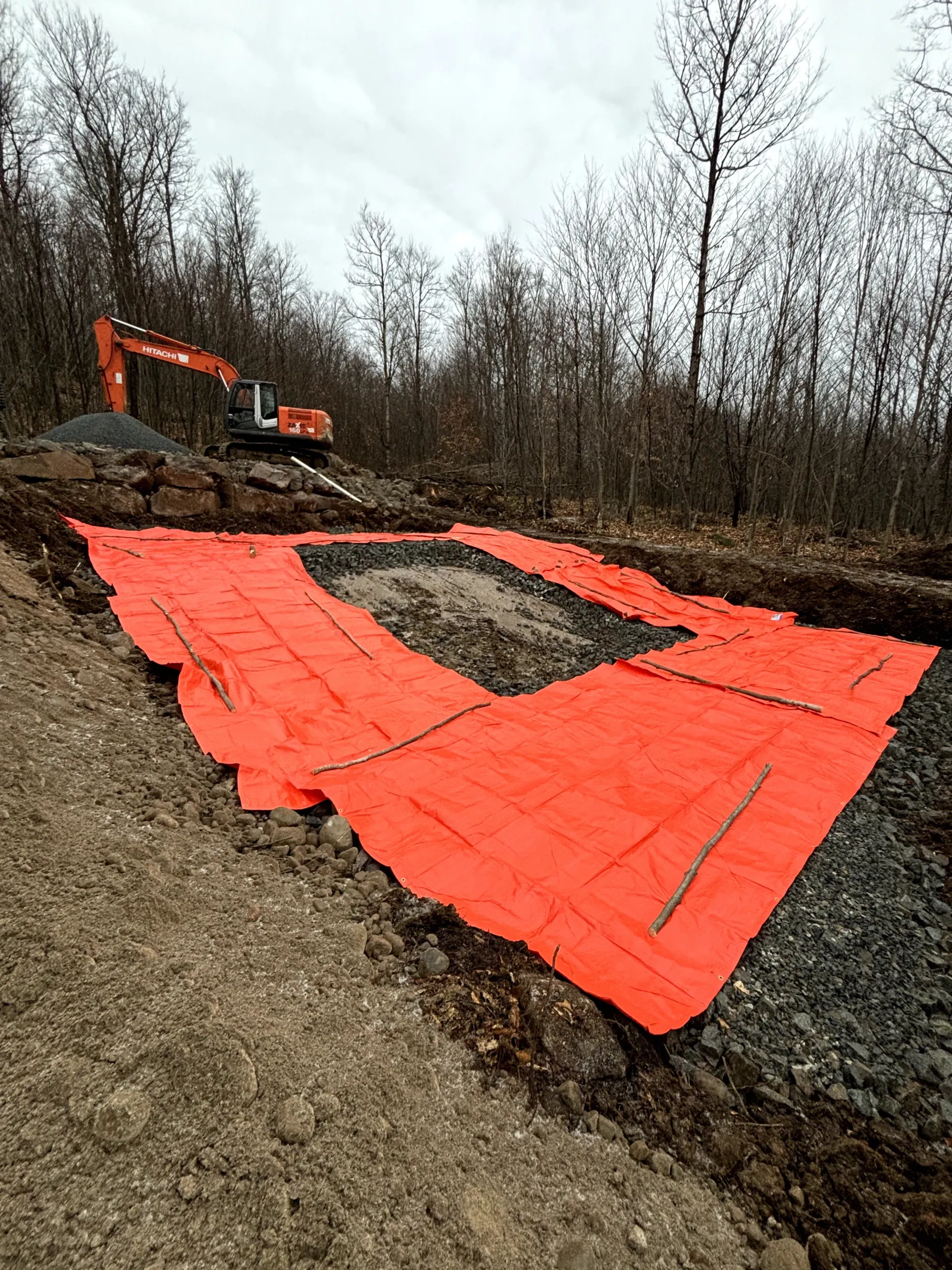 Orange erosion-control mats on a muddy hillside with an excavator in the background