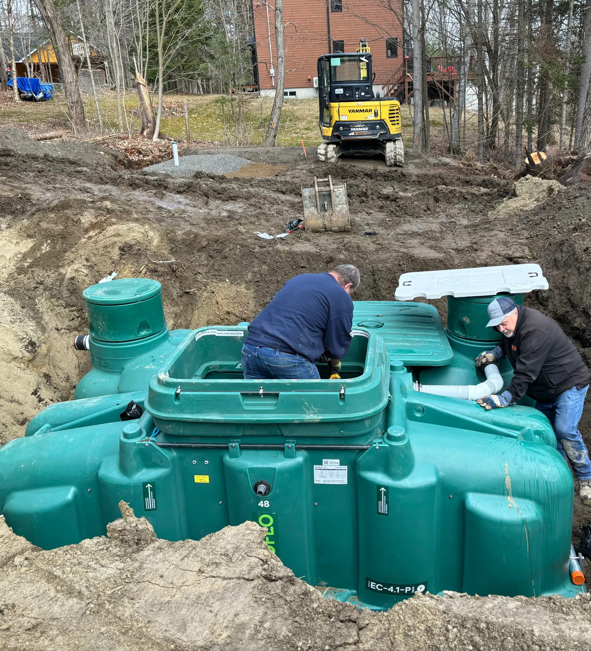 Workers installing a large green underground tank at a muddy construction site