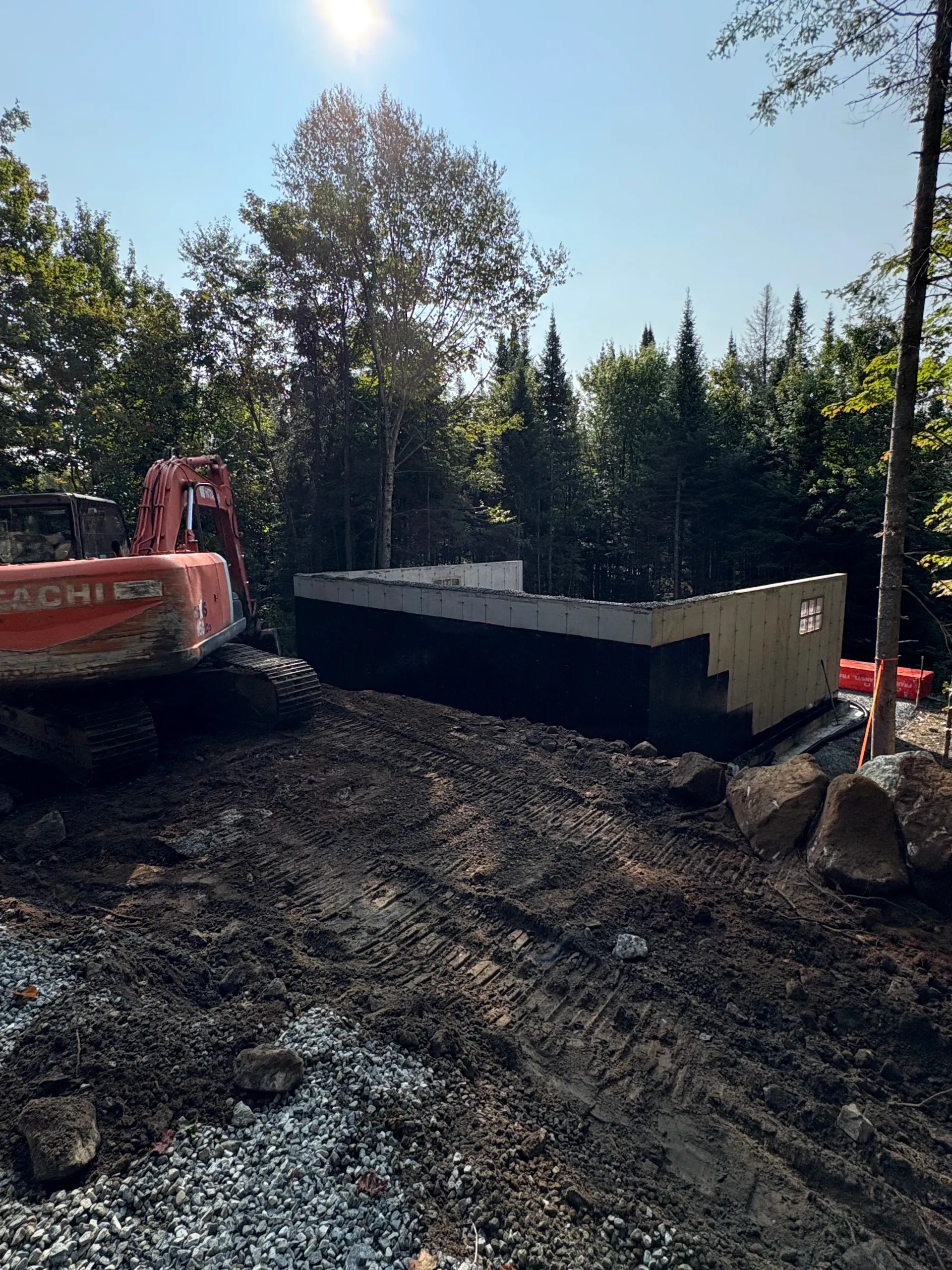 Excavator at a construction site beside a partially built concrete foundation in a wooded area