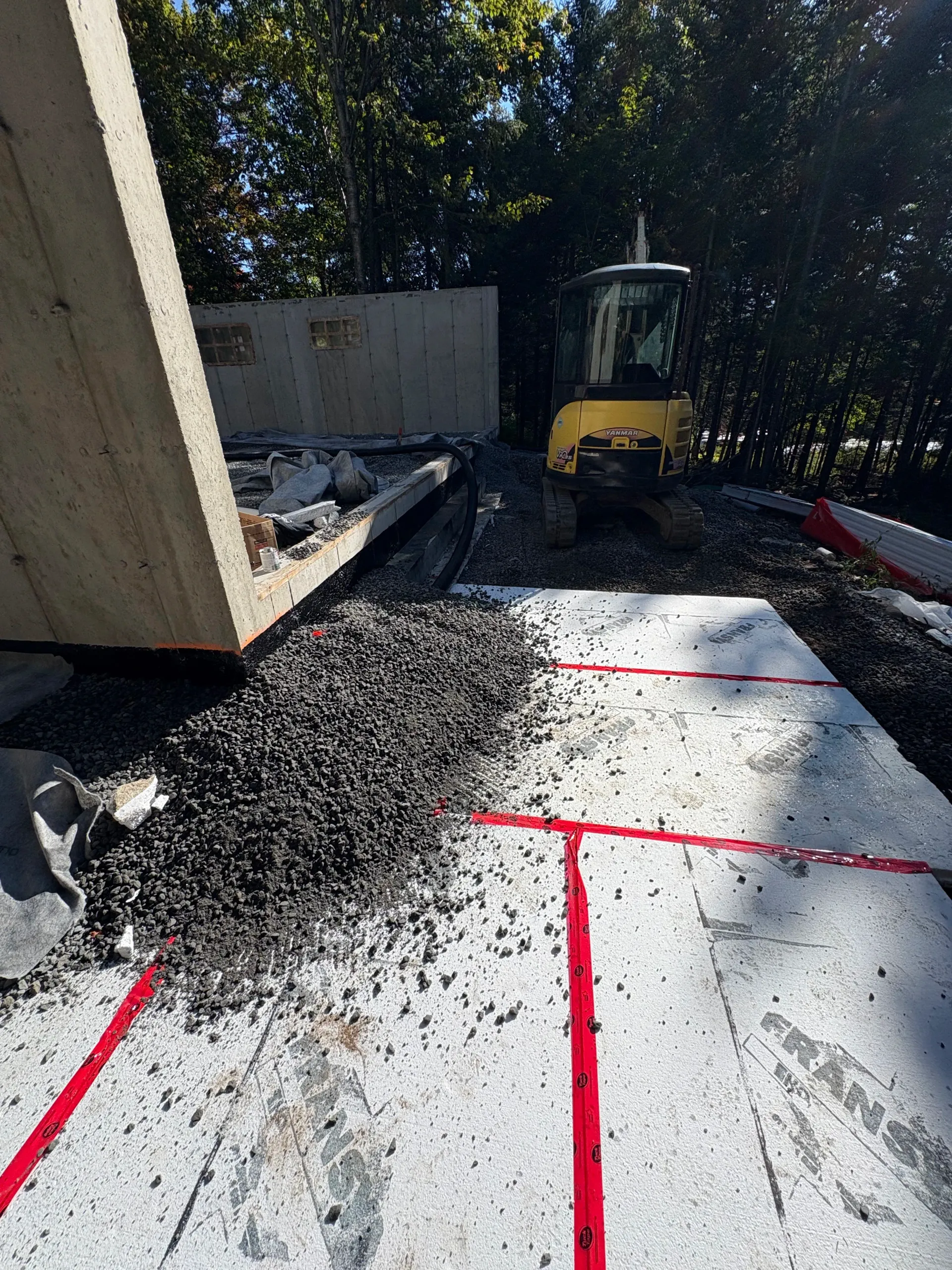 Construction site with yellow excavator and fresh concrete marked with red lines near a building wall