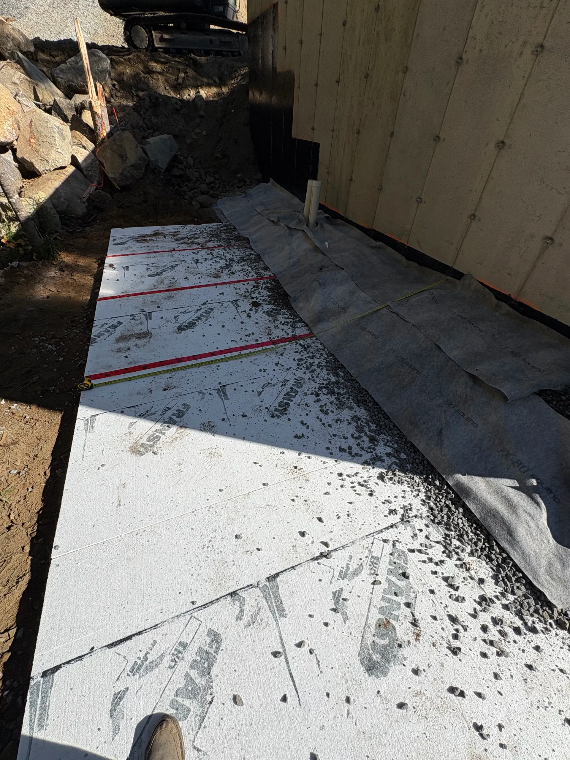 Narrow concrete walkway beside a building, with rocks on one side and strong sunlight casting shadows.