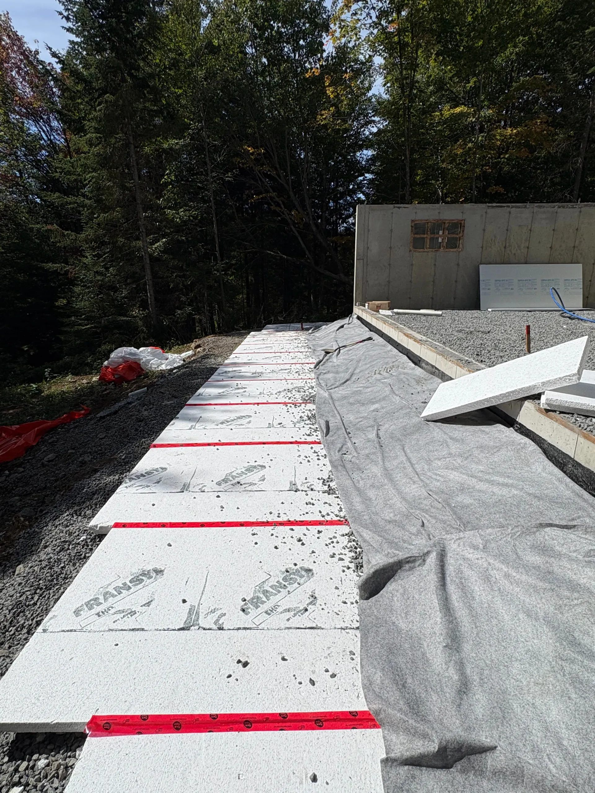 Concrete walkway under construction beside a building, with red markings and gravel edging.