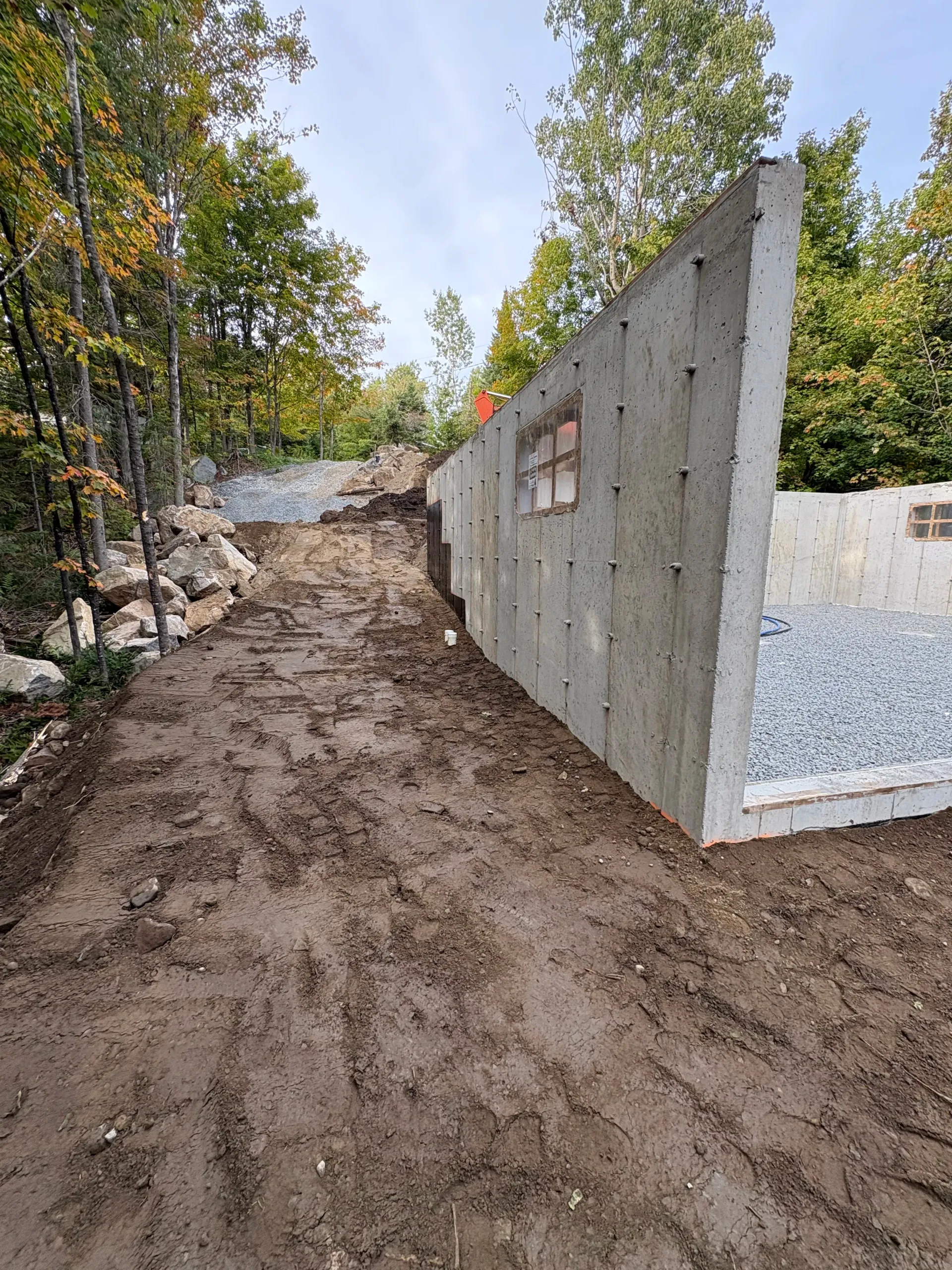 Muddy construction site with concrete walls and trees along a dirt path