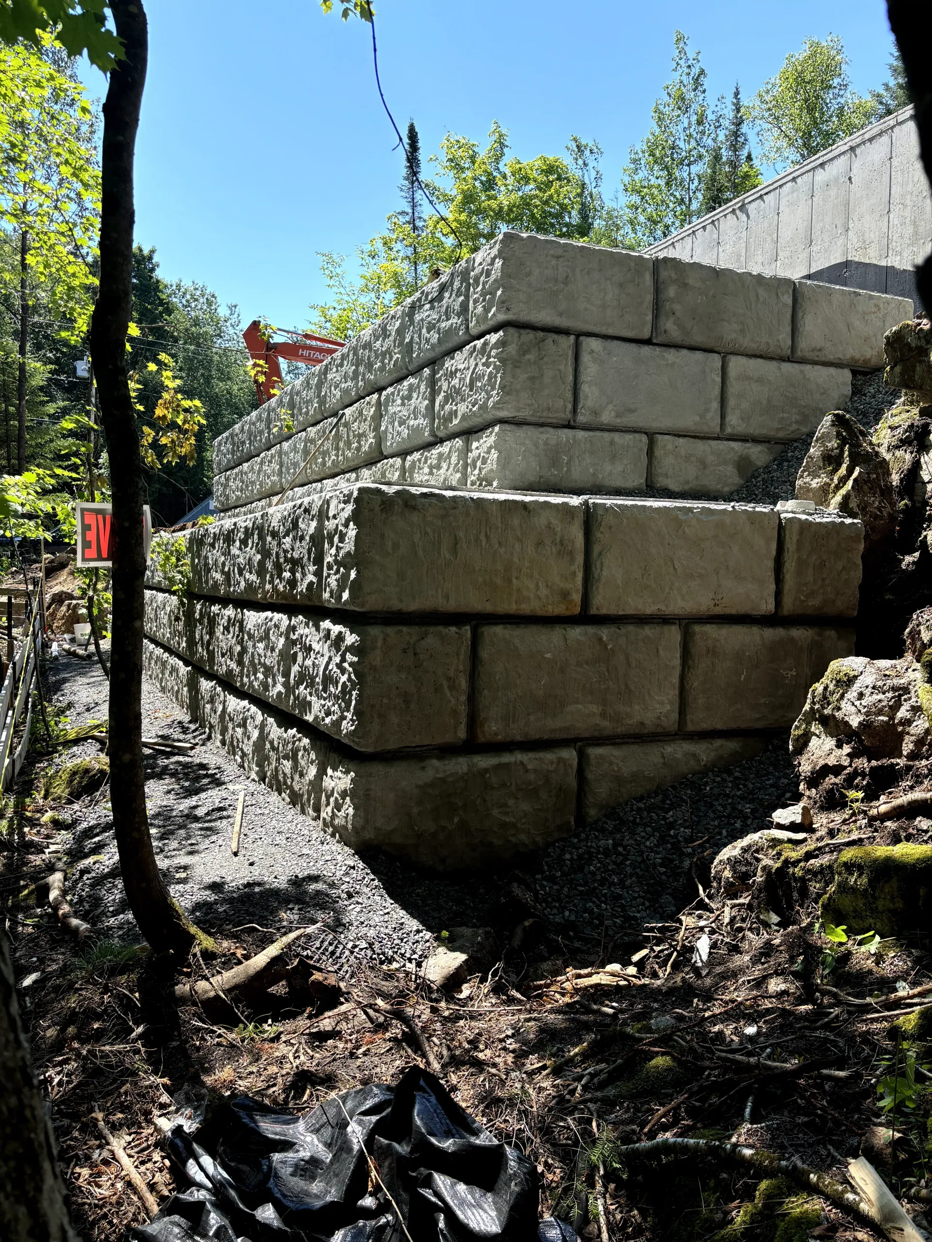 Stacked cinder blocks forming a retaining wall on a rocky slope in a sunny wooded area.
