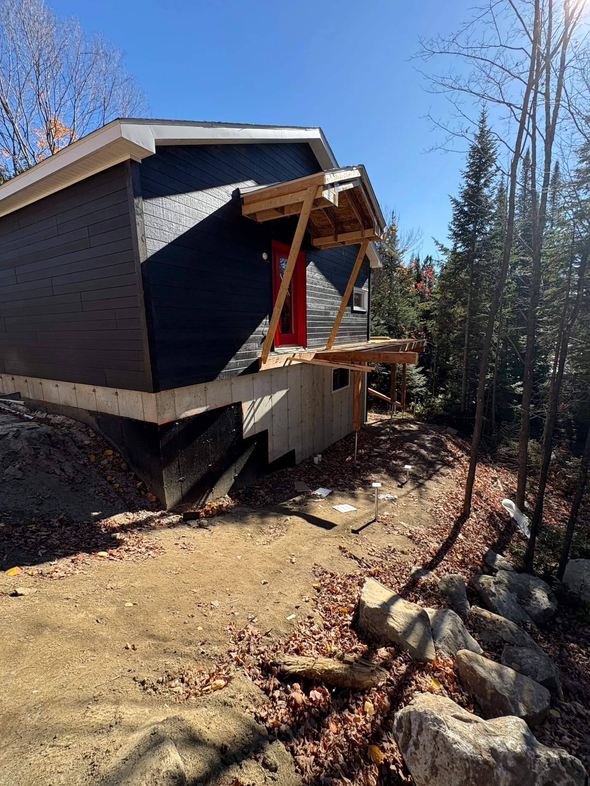 Small cabin with a front porch under construction in a wooded area, with rocks lining the path.