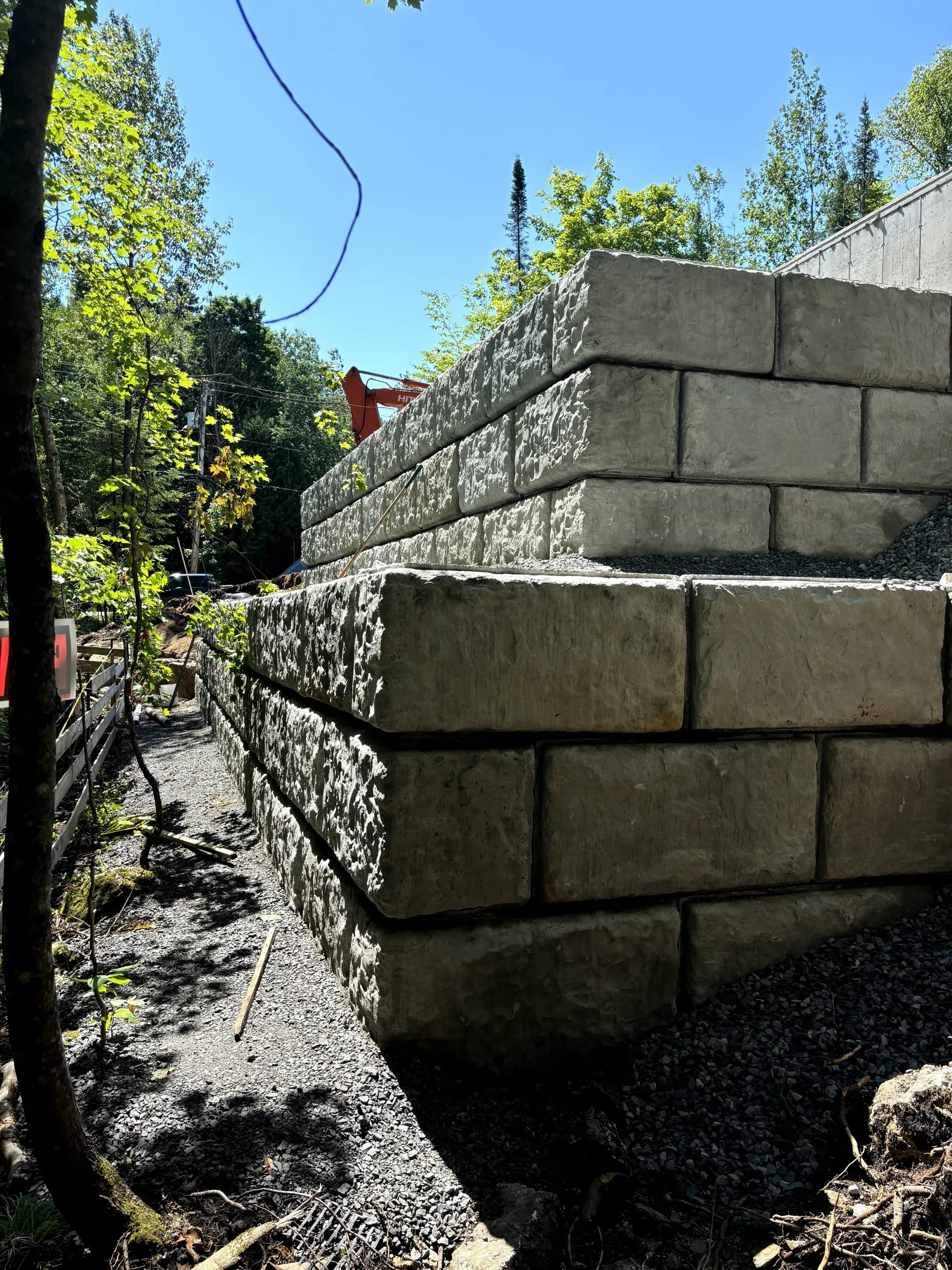 Stacked concrete blocks forming a retaining wall beside a gravel path in a sunny outdoor area.