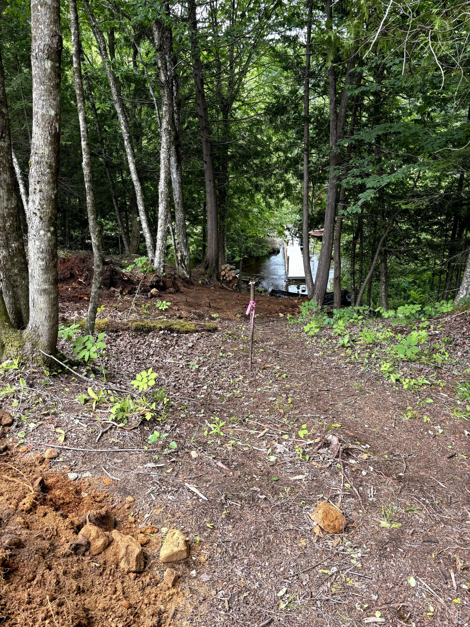 Construction site with gravel pad, white drainage pipes, and an excavator near a wooded area