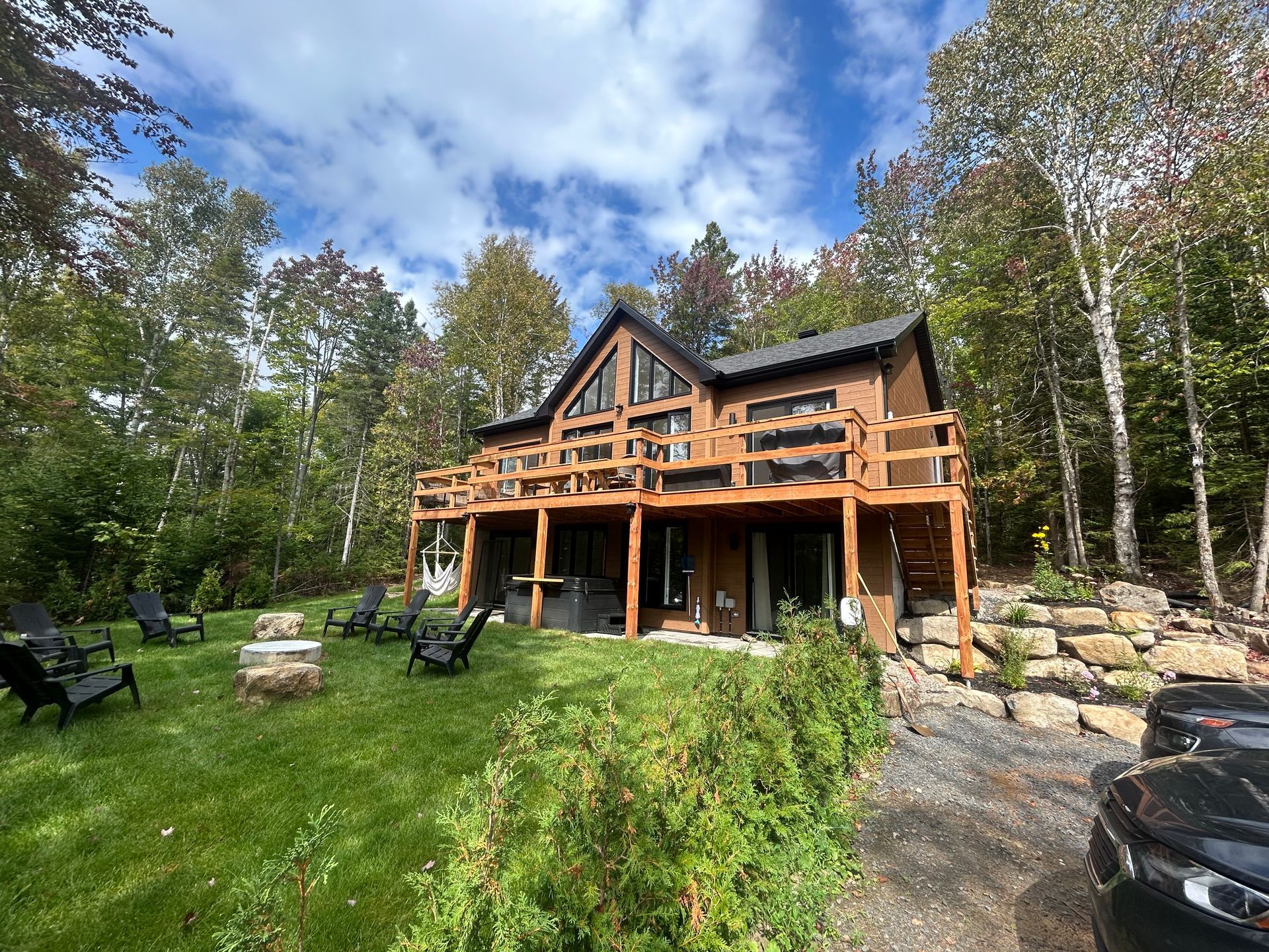 Wooden cabin with a large deck in a wooded yard under a blue sky