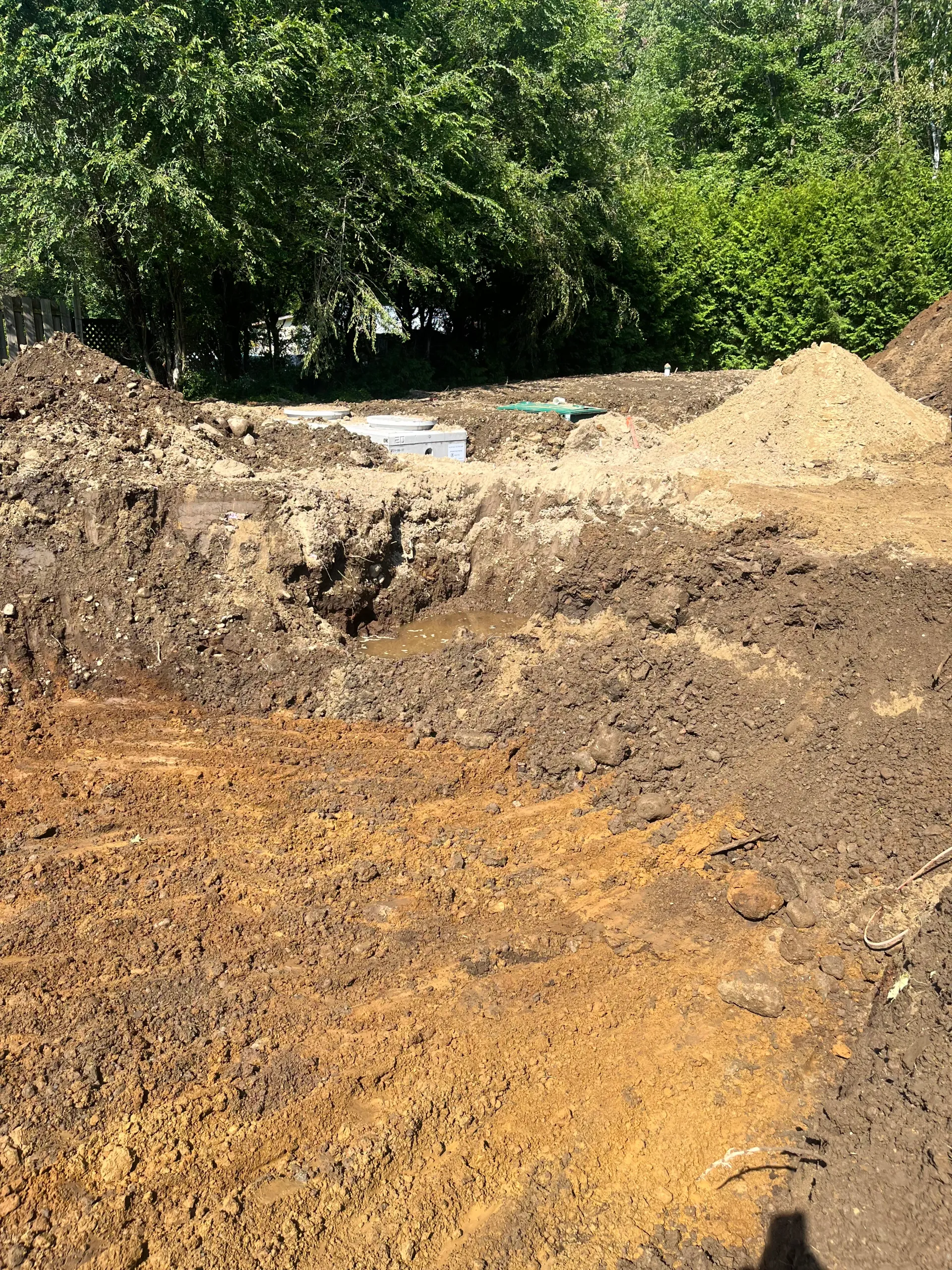 Dirt excavation site with mounds of brown soil and dense green trees in the background