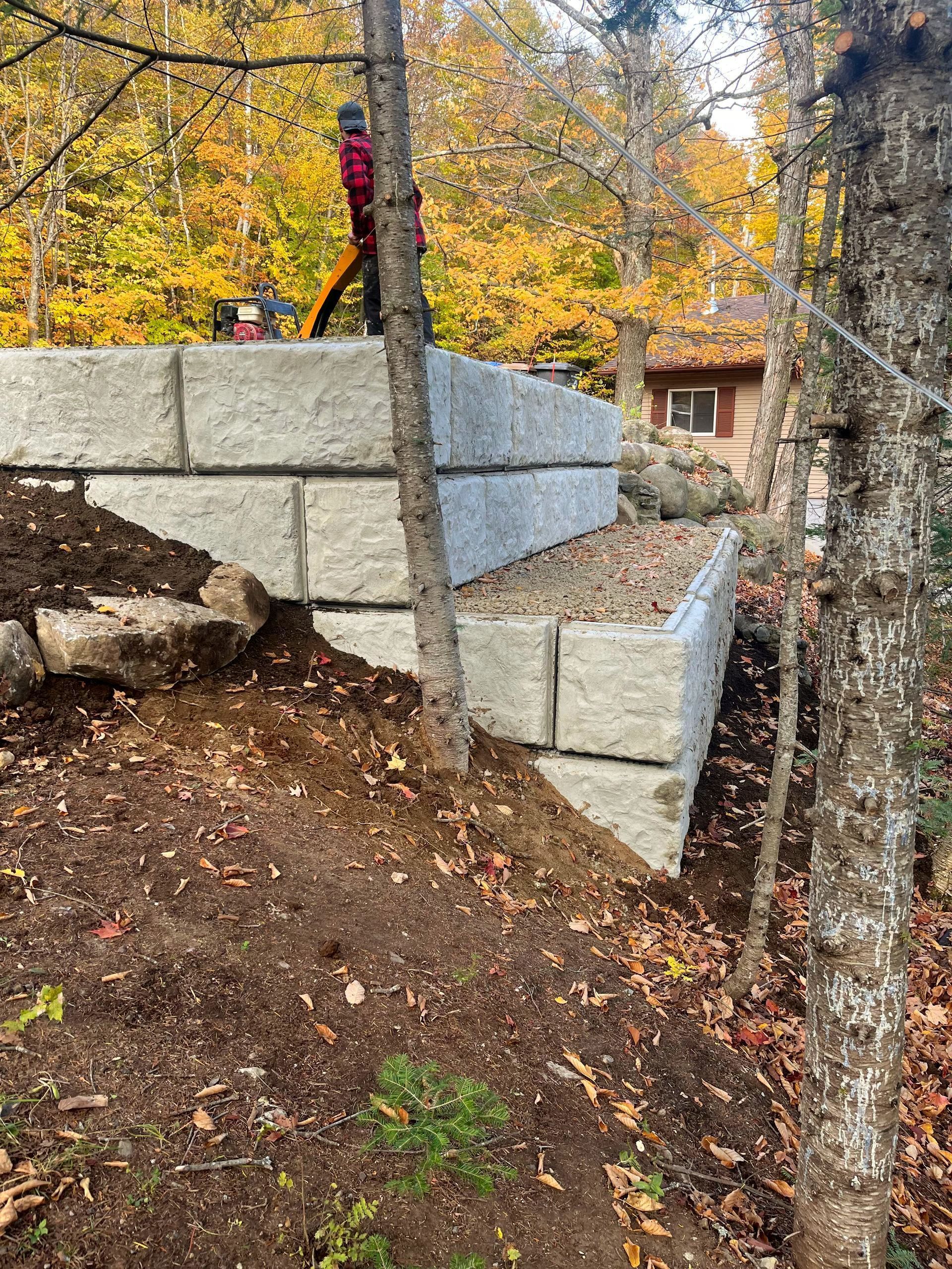 Stone retaining wall on a wooded slope in autumn, with a person in red standing above it.