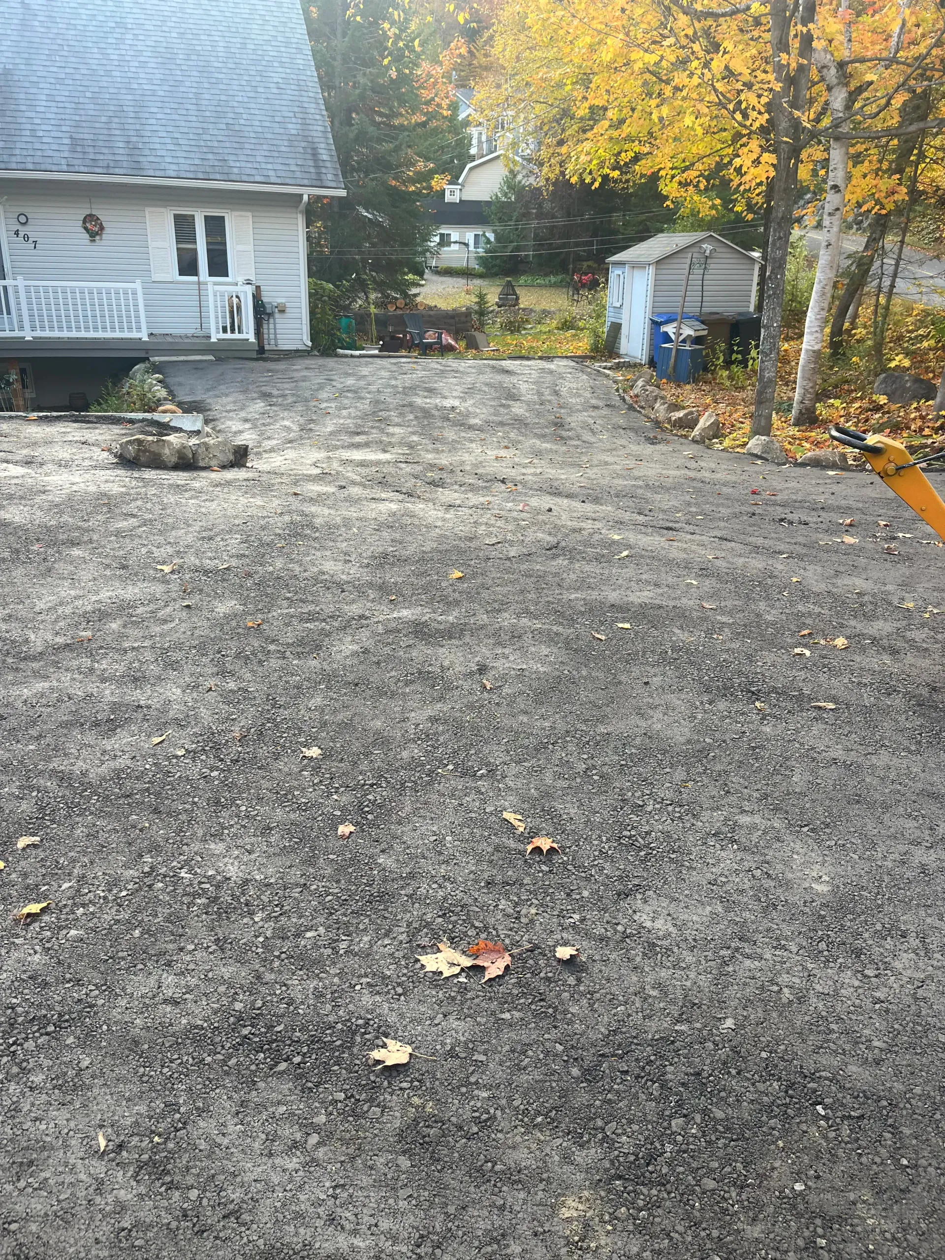 Gravel driveway beside a white house with autumn trees and a small shed.