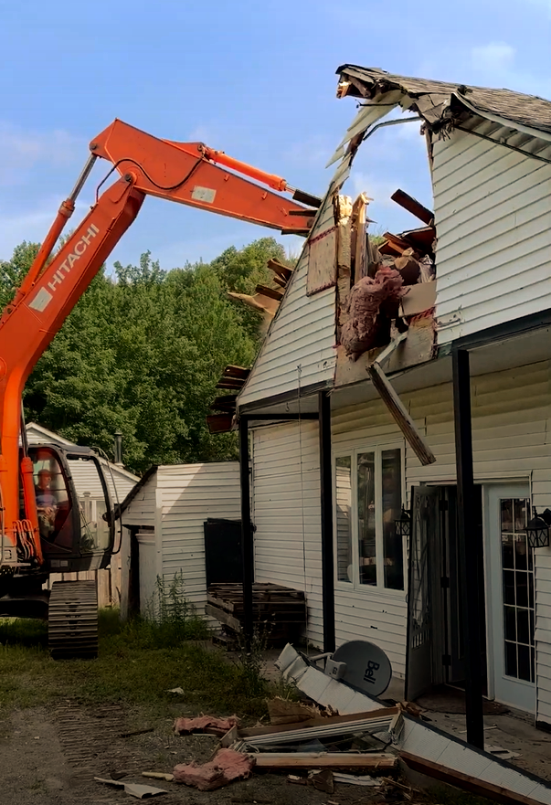 Excavator demolishing the roof of a white house during renovation