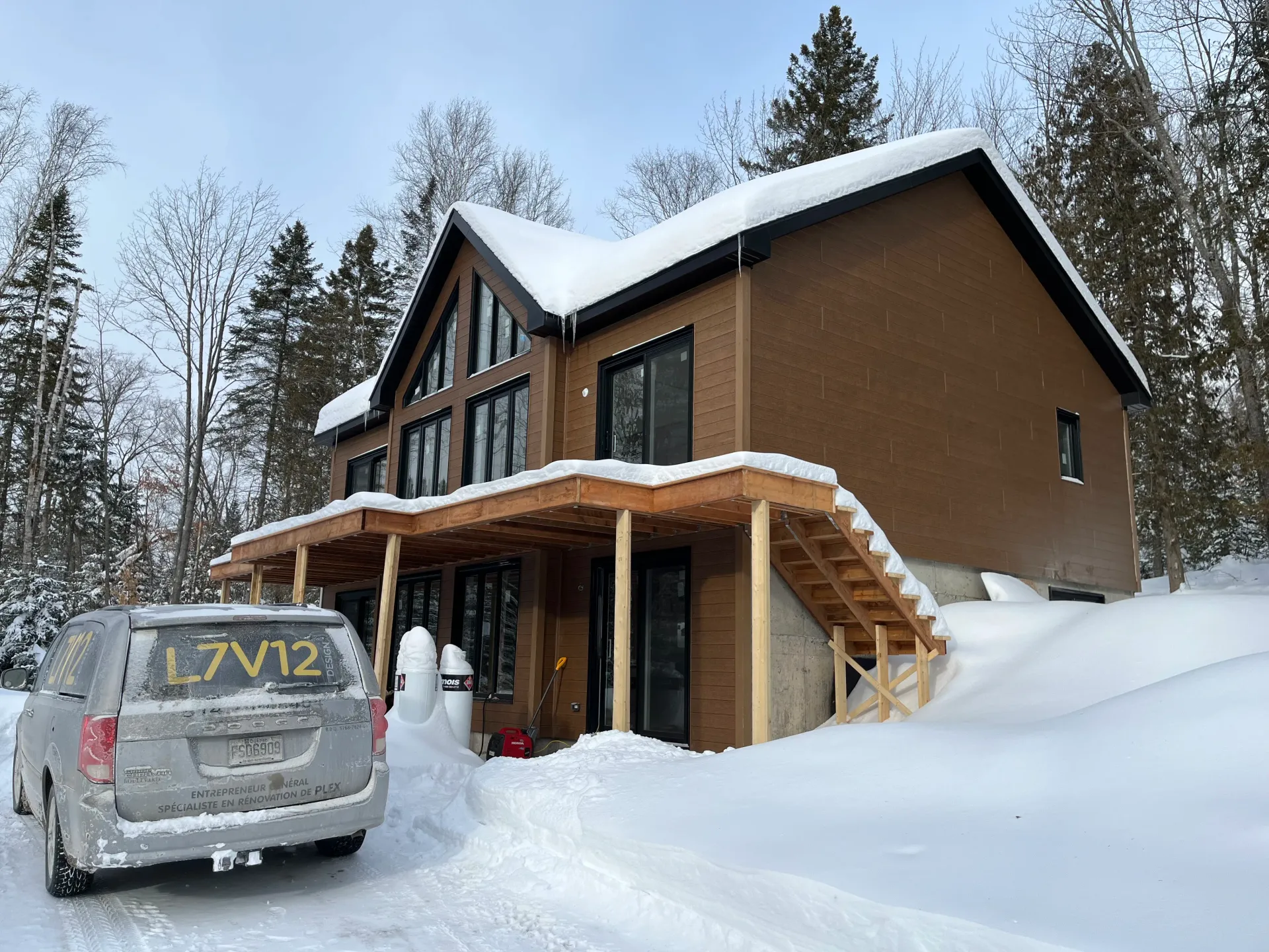 Snowy modern cabin under construction with a van parked in front
