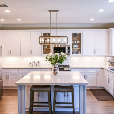 A kitchen with white cabinets and a large island with a vase of flowers on it.