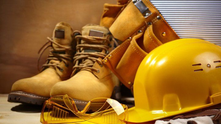 A pair of boots , a hard hat , safety glasses , and a tool belt are on a table.