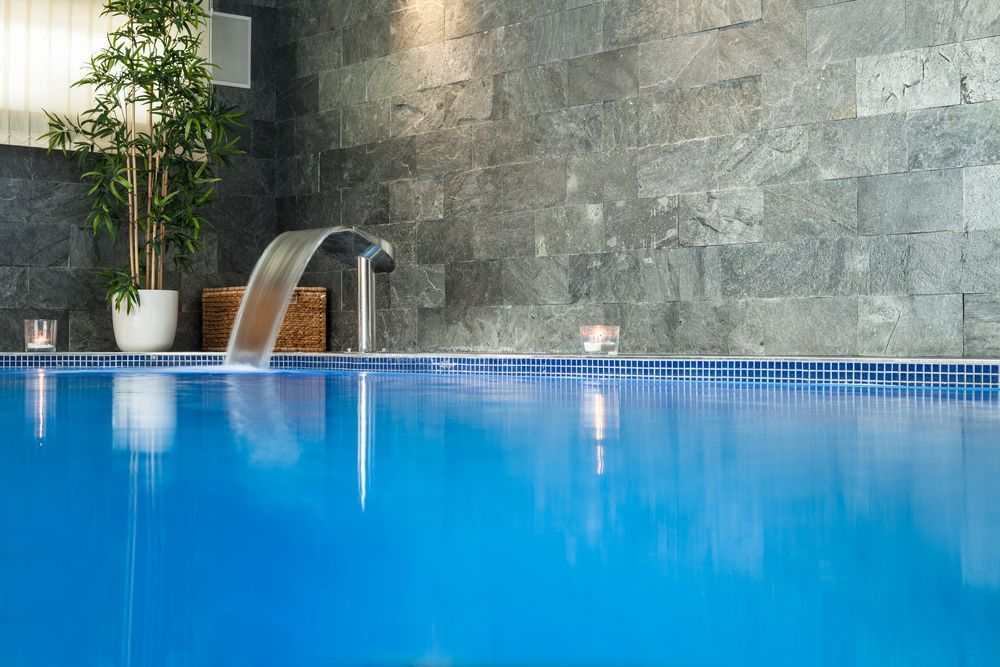 A Blue Indoor Swimming Pool With a Stone Wall — Sun Cool Pools & Spas in Maryborough, QLD