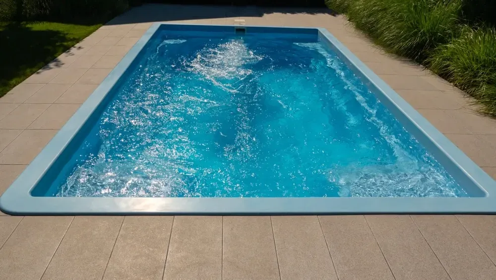 A Rectangular Blue Swimming Pool Set in a Paved Backyard Patio — Sun Cool Pools & Spas in Bundaberg, QLD