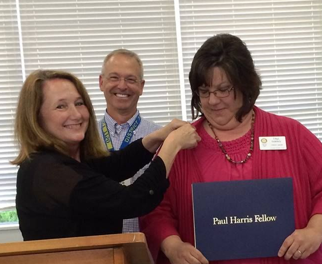 Three people at a podium, smiling, with one woman holding a Paul Harris Fellow plaque.