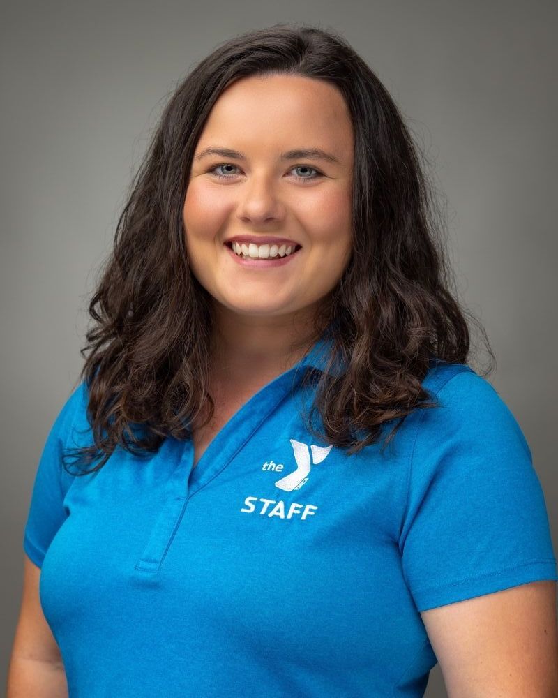 Smiling staff member in a blue polo shirt against a gray background