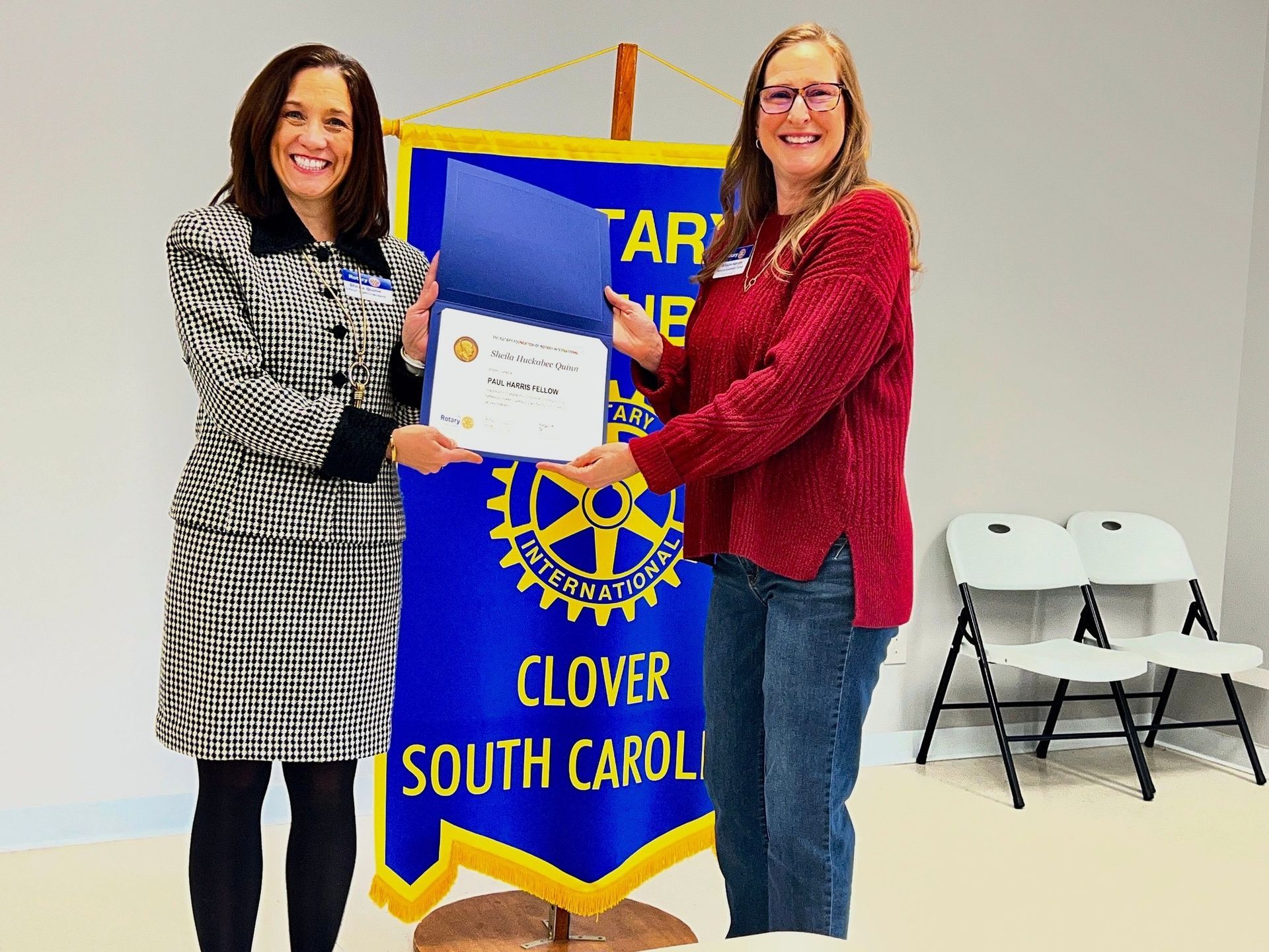 Two women holding a certificate beside a blue Clover South Carolina Rotary banner