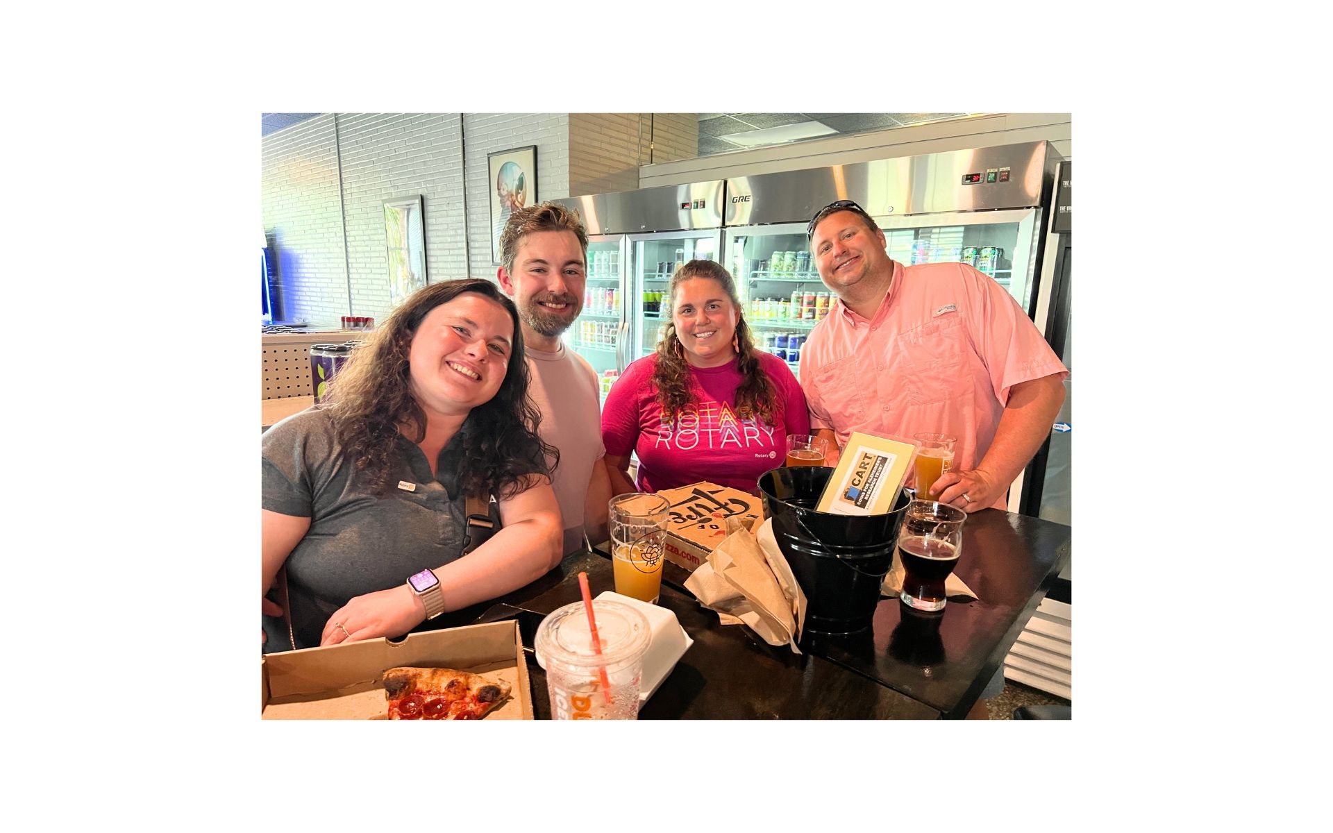 Four smiling friends at a table in a bright café, with drinks and a gift bag.