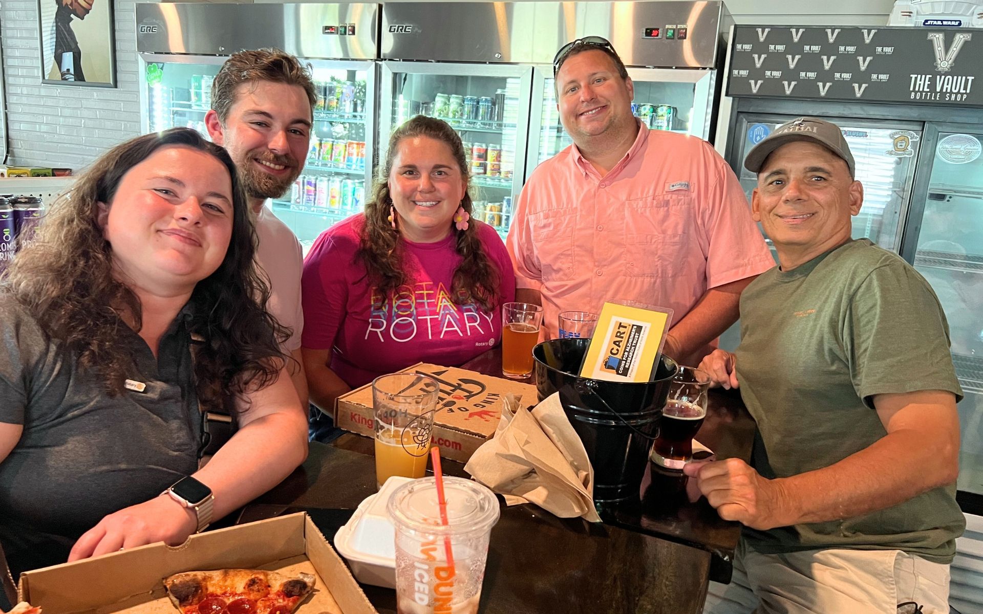 Five friends smiling at a restaurant table with drinks and takeout boxes