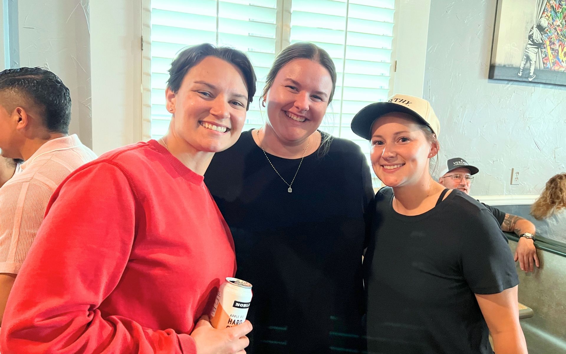 Three people smiling indoors, posing together at a gathering.