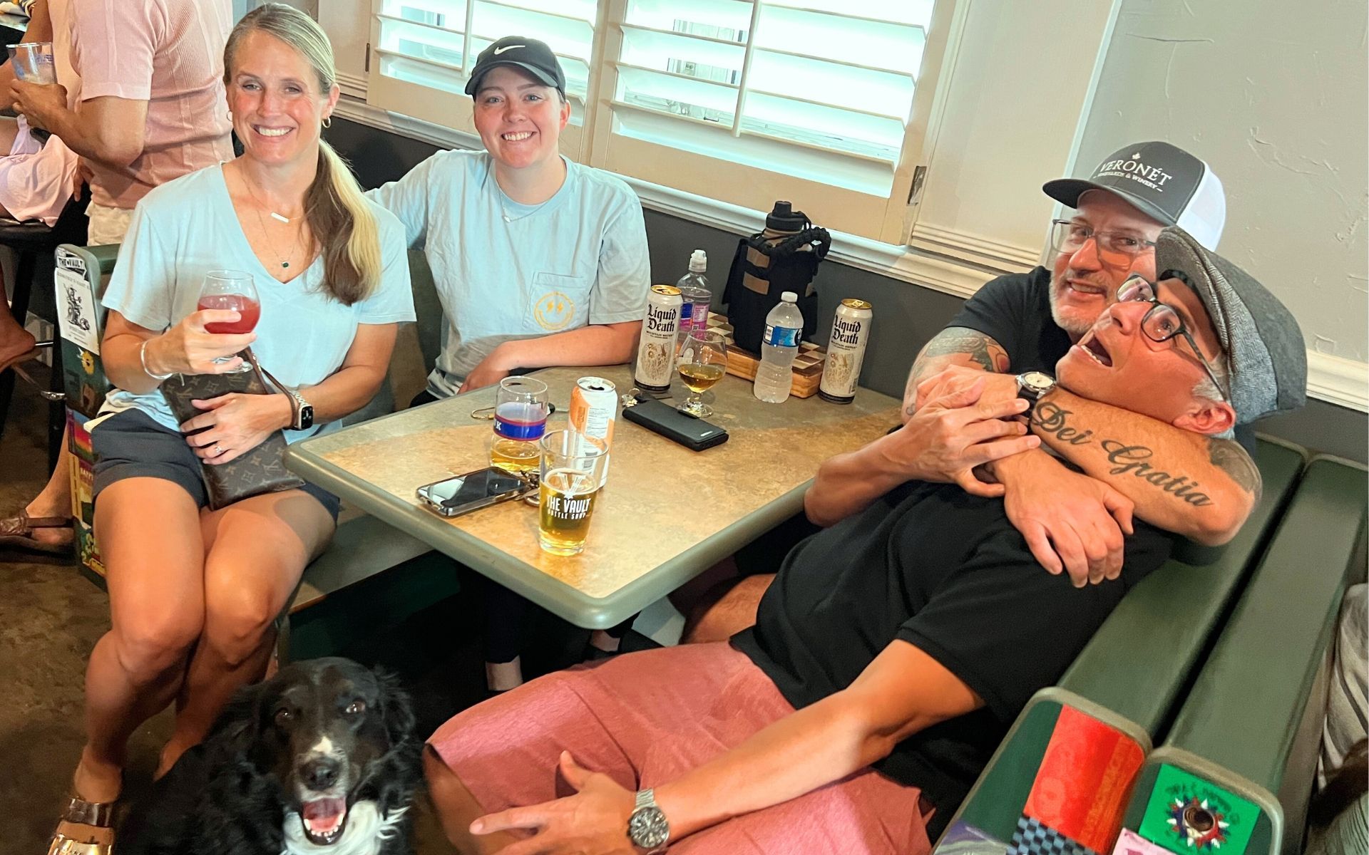Friends sitting in a booth at a restaurant with a dog on the floor and drinks on the table