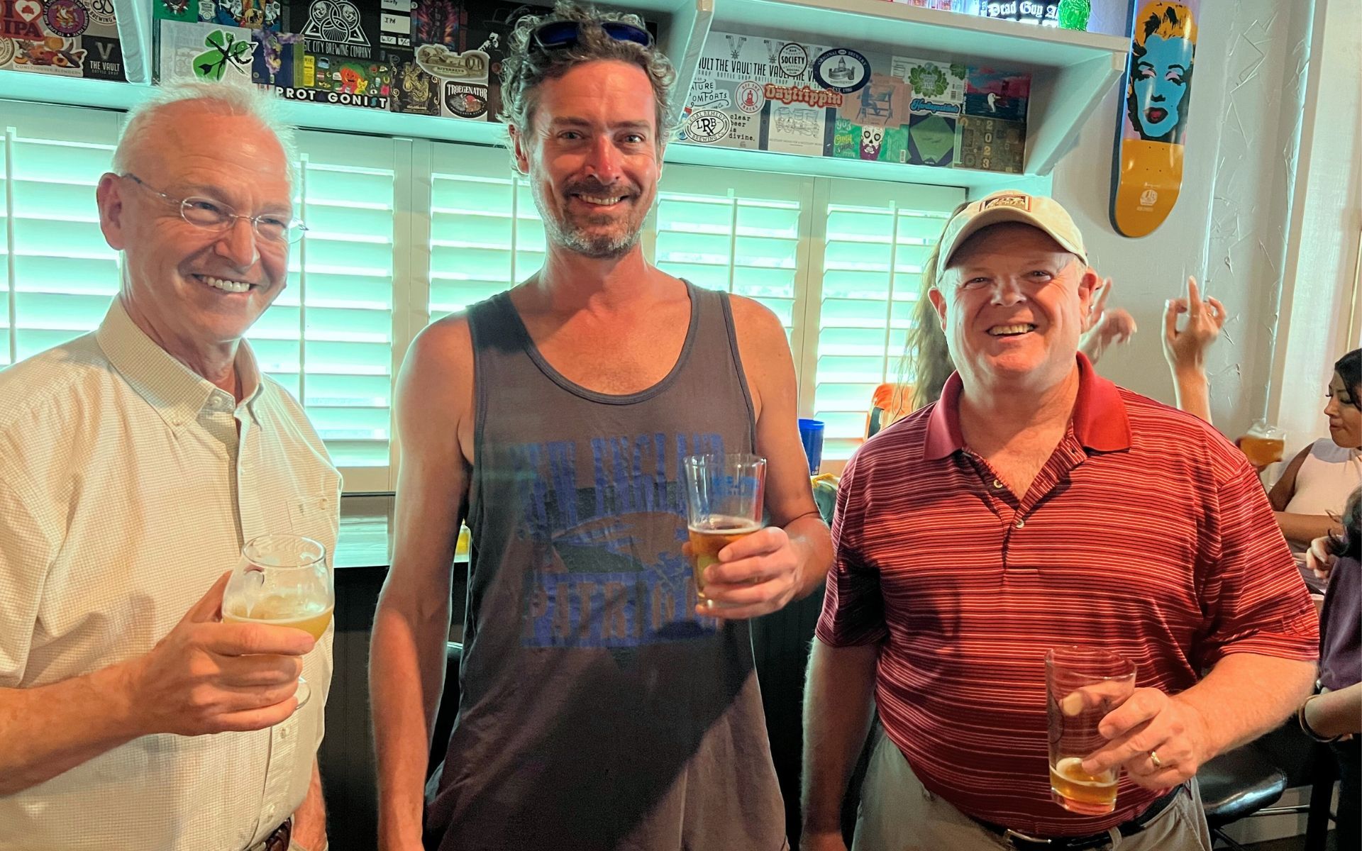 Three smiling people holding drinks in a colorful indoor bar or restaurant.