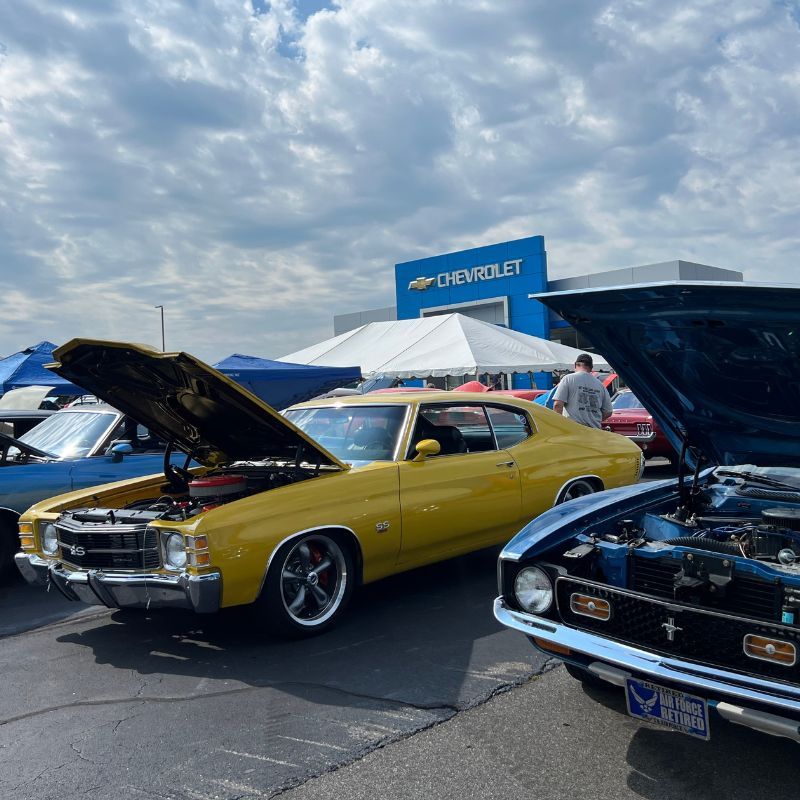 Classic yellow and black Chevy cars with open hoods at a Chevrolet car show