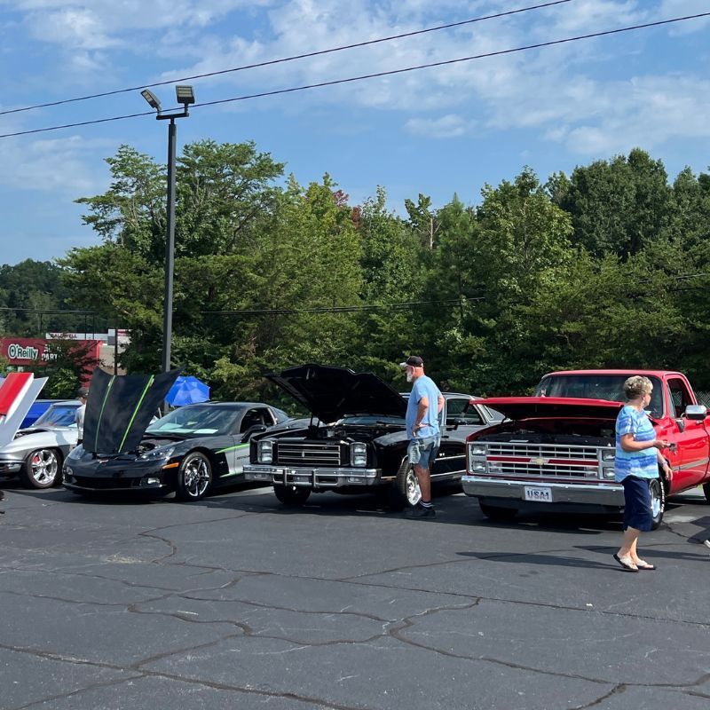 Classic cars on display at an outdoor show, with two people standing beside open-hood vehicles.
