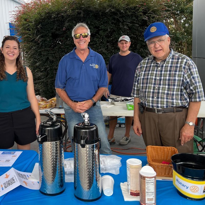 People standing behind a table with coffee carafes and cups at an outdoor event