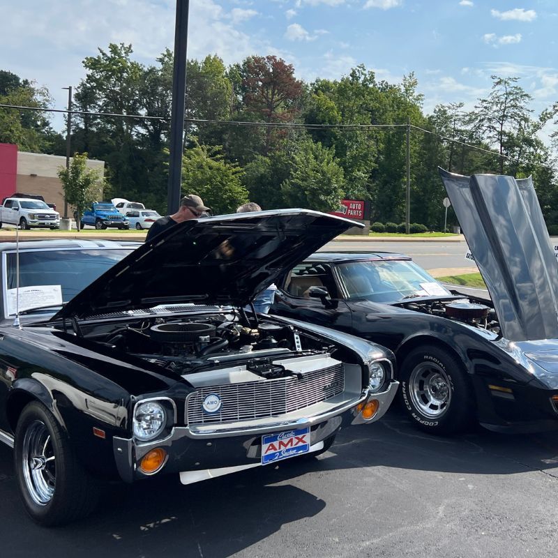 Two classic black muscle cars on display with hoods open in a parking lot