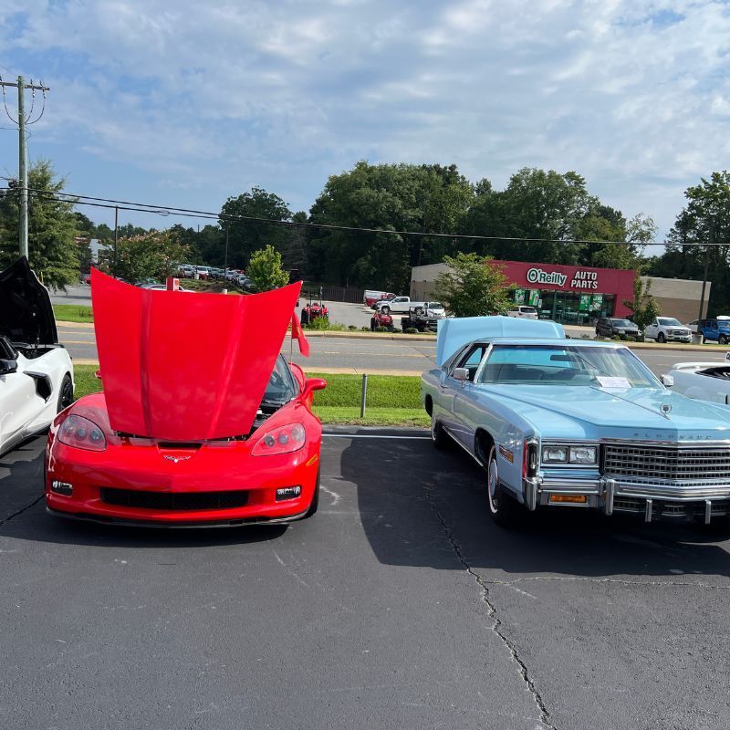 Red sports car with hood open beside a light blue classic car in a parking lot at a car show