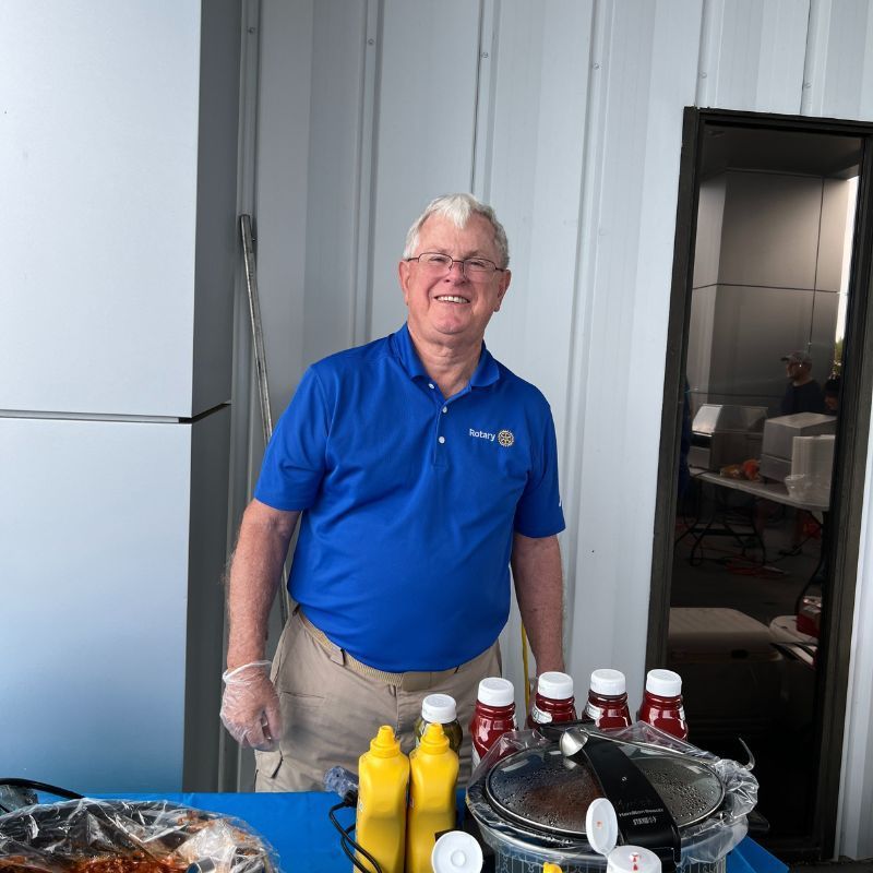 Smiling man in blue polo standing behind table with bottled drinks and snacks in a kitchen area