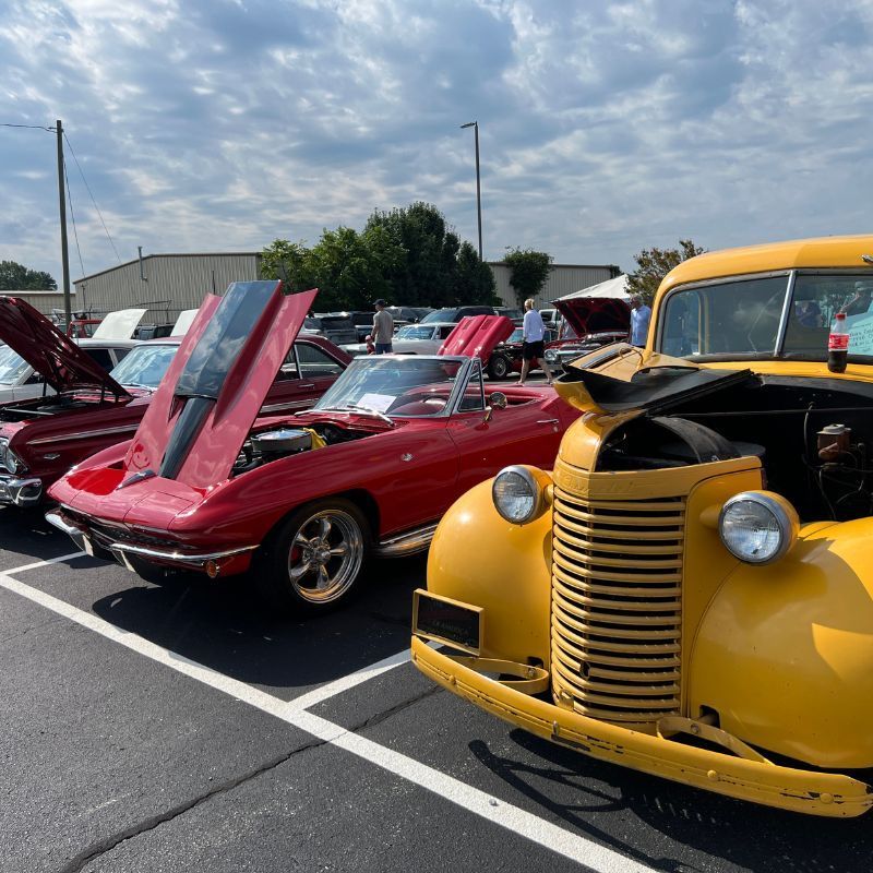 Classic cars at a show, including a red convertible and yellow vintage truck with open hoods.